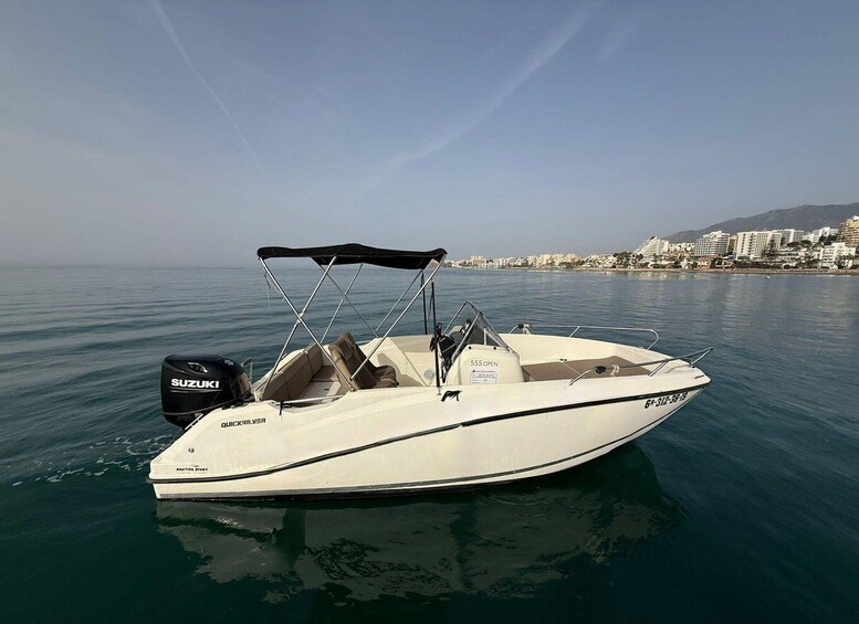 A white motorboat named QUICK SILVER with a Suzuki outboard motor, docked in calm waters with a coastal cityscape in the background. 2