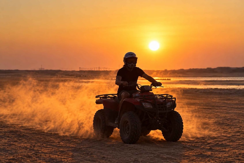 A person riding an ATV on a sandy terrain during sunset. 2