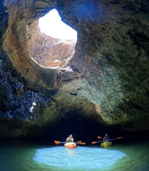 Two kayakers inside a cave with a natural opening to the sky. 4