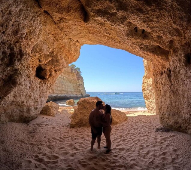 A couple standing in a cave opening with a beach and cliffs in the background. 2