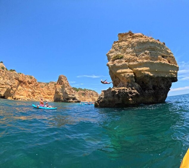 A person diving off a cliff into the sea, a kayak with two people, and rocky cliffs. 3