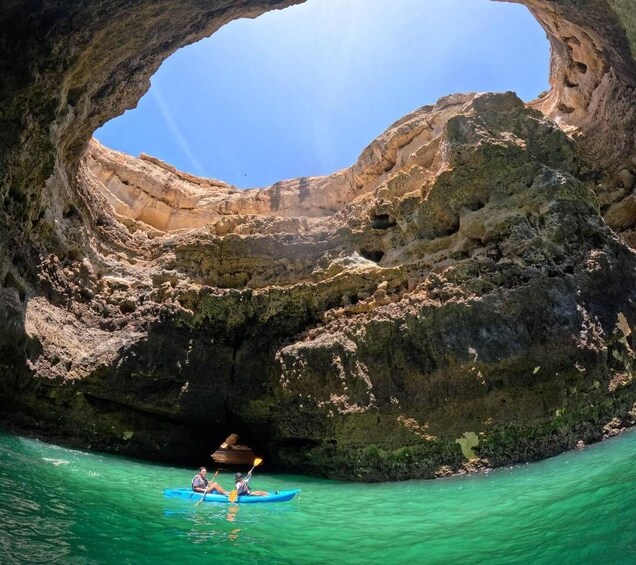 A kayaker in a blue kayak navigating through a turquoise sea under a large rock arch. 5
