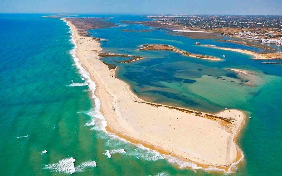 An aerial view of a coastal area with a sandy beach, clear blue waters, and a distant urban settlement. 1