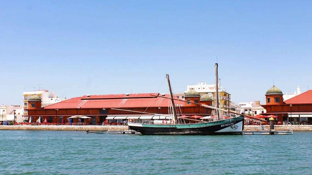 A traditional fishing boat docked at a harbor with buildings in the background. 4