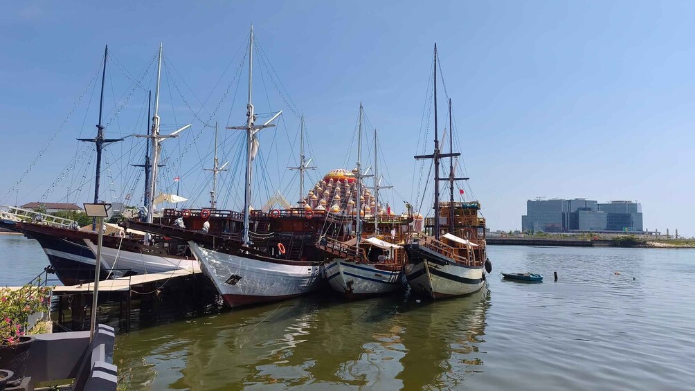 A fleet of sailing ships docked at a marina with a modern building in the background. 1
