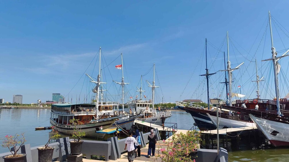A marina with several tall ships docked, a clear blue sky, and a cityscape in the background. 2