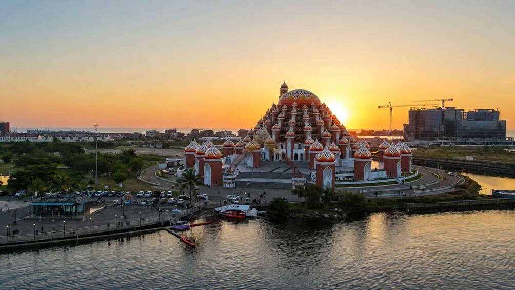 A large, ornate building with multiple domes, situated by a waterfront with boats docked. 1