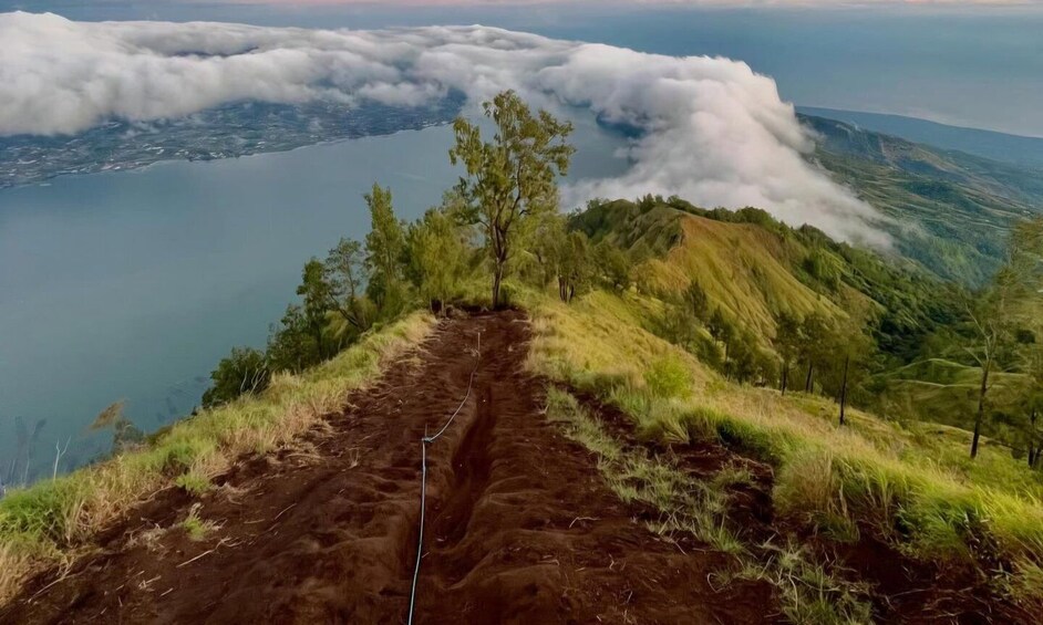 A dirt path leading to a mountain peak with a view of a lake and clouds below. 4