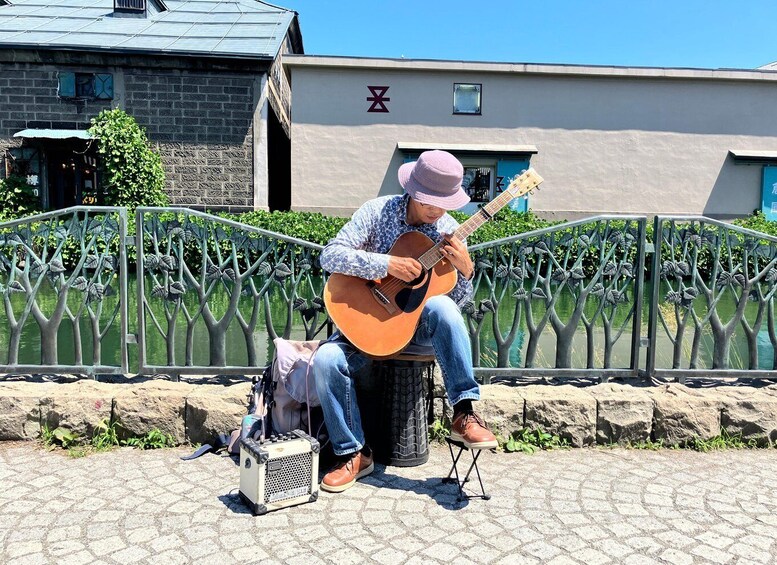 A person playing an acoustic guitar on a stone bench near a decorative fence. 1