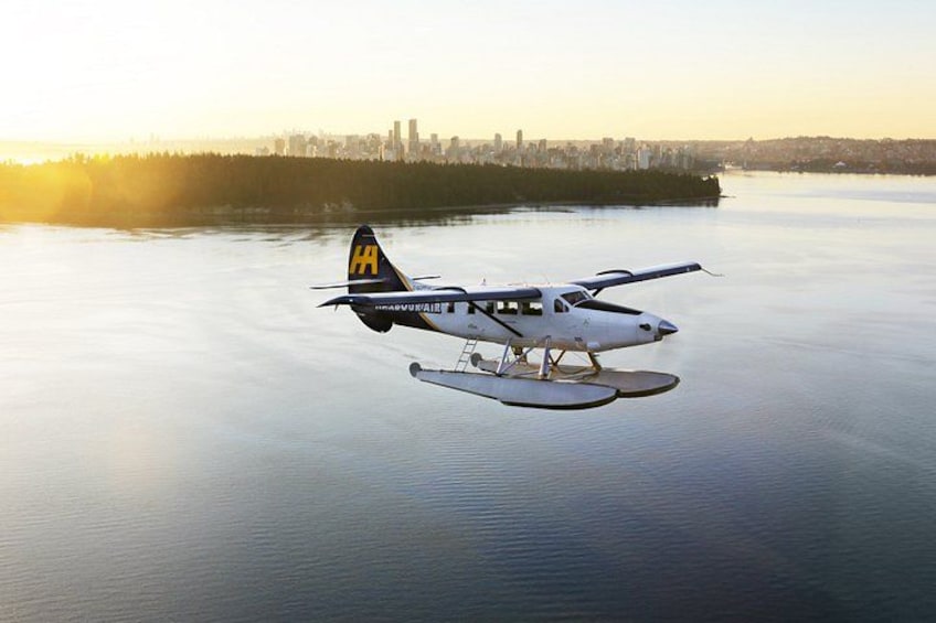 Un hidroavión con pontones vuela sobre aguas tranquilas, con el horizonte de una ciudad al fondo. 1