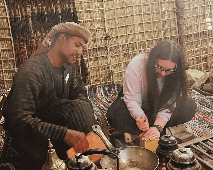 Two people in traditional attire, one cooking with a pot and another preparing food. 2