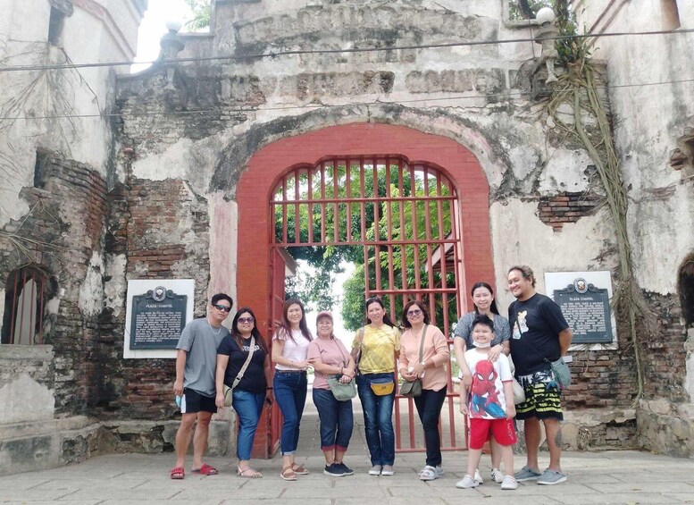 A group of people standing in front of an old building with a red gate and two informational plaques. 5