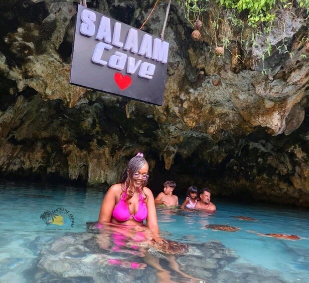Eine Höhle mit einem Schild, auf dem 'Salah Cave' steht, und einer Frau in einem pinkfarbenen Badeanzug. 2