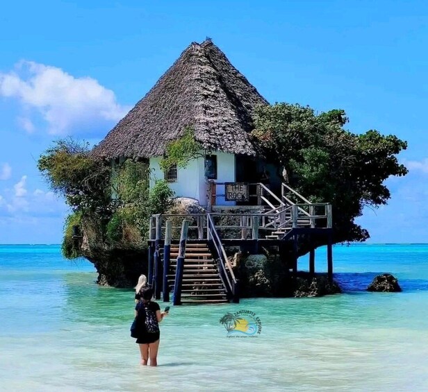 Ein Haus mit Strohdach auf Stelzen über türkisfarbenem Wasser. 1