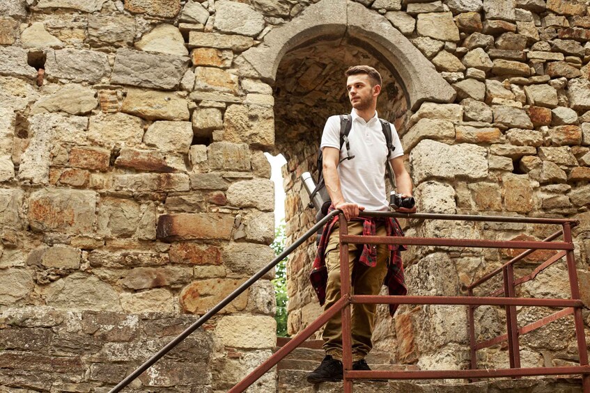A person on a metal scaffold in front of a stone wall with an arched doorway. 3