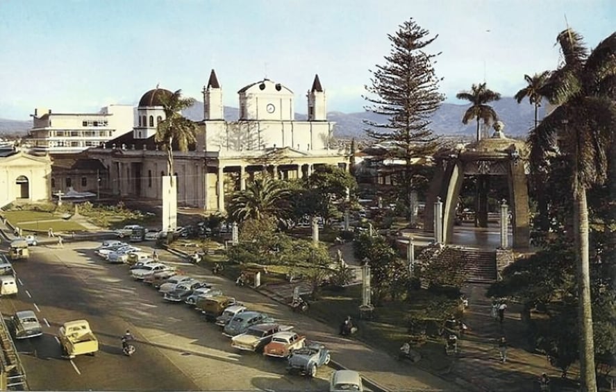 A cityscape with a prominent church, parked cars, and palm trees. 3