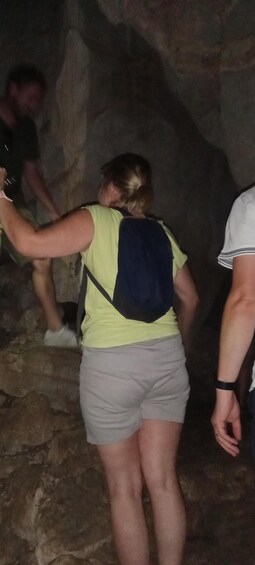 En person som bär en gul skjorta och grå shorts, och som har en blå ryggsäck på sig, står i en grotta med steniga väggar. 5