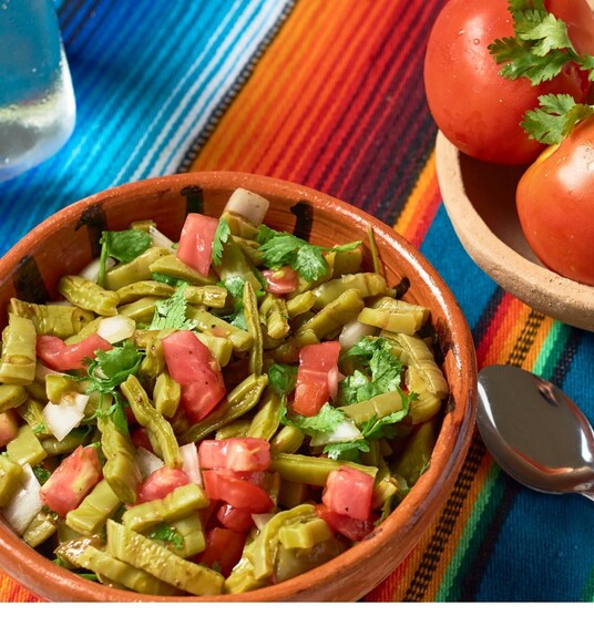 A bowl of green vegetables and tomatoes with cilantro, on a colorful cloth. 1