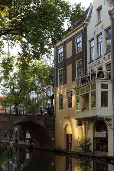 A canal with a bridge, buildings with signage, and a tree reflecting in the water. 5