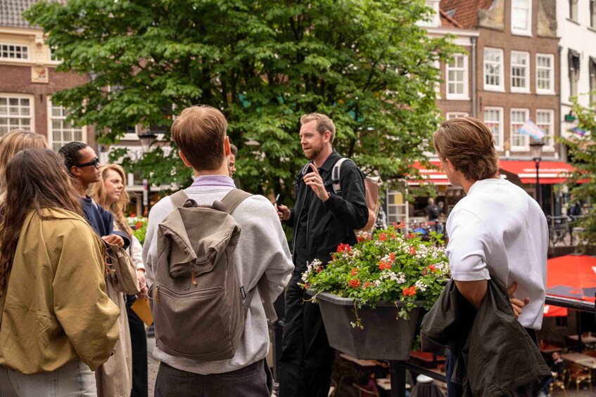 A group of people standing outdoors, some with backpacks, in an urban setting with buildings and a flower cart in the background. 4