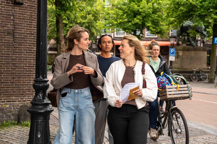 Three people conversing on a city sidewalk, with a bicycle and a park sign in the background. 3