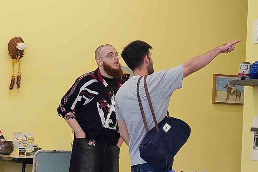 Zwei Personen in einem Raum mit einer gelben Wand, einer Uhr und einem gerahmten Bild. 3