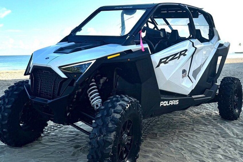 En Polaris RZR på en sandstrand med oceanen i baggrunden. 3