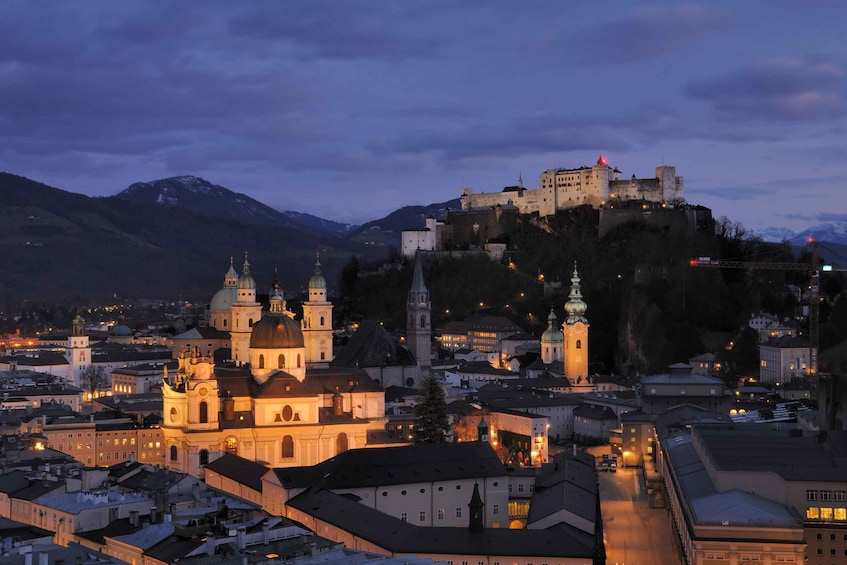 A historic city with a prominent castle on a hill, surrounded by buildings and a mountain range. 3
