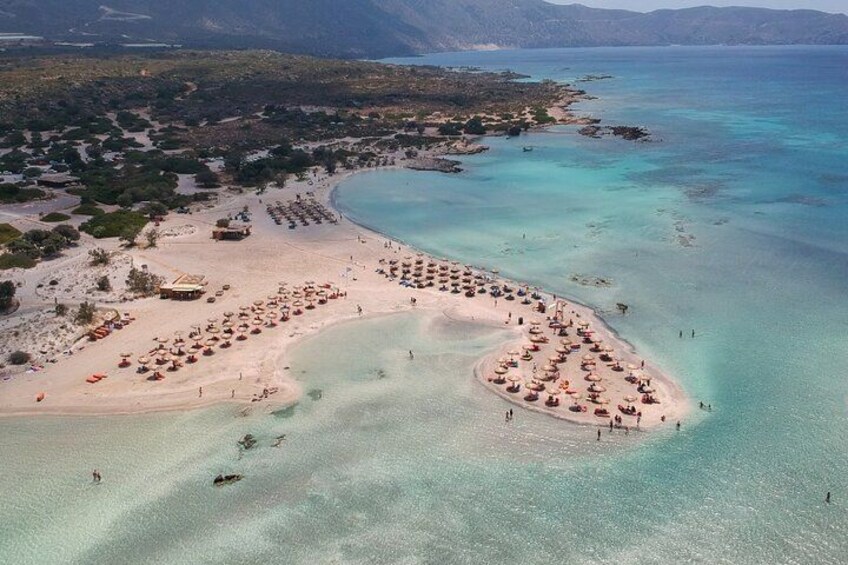 An aerial view of a beach with clear turquoise waters, a crescent-shaped sandbar, and a small island with umbrellas. 2