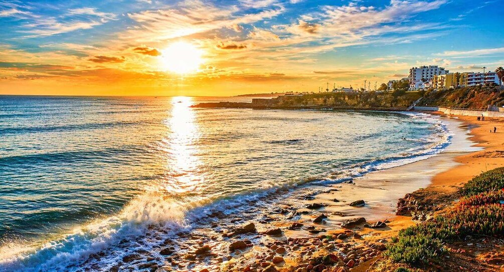 A sunset over a beach with waves, a sandy shore, and buildings in the background. 1