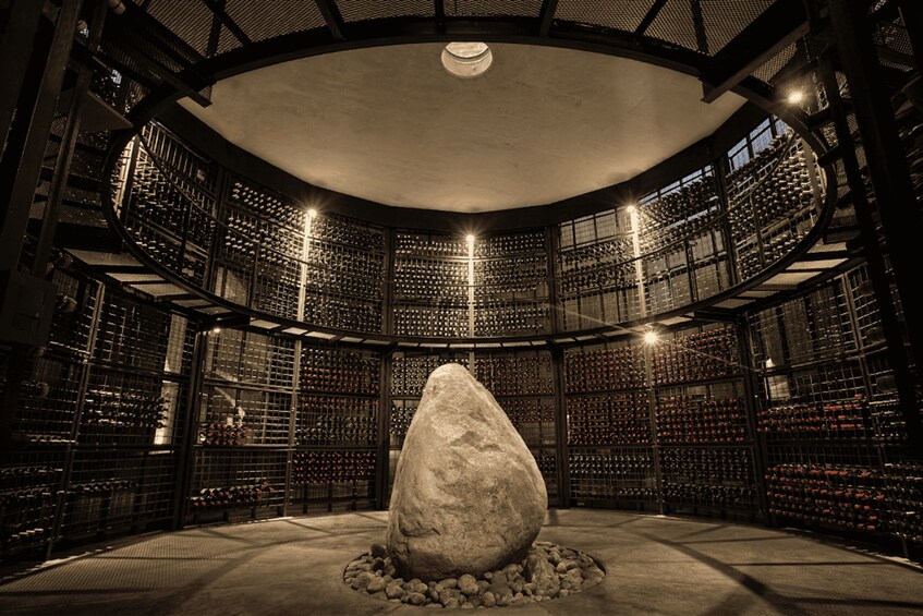 A circular room with a large stone centerpiece surrounded by shelves of wine bottles. 2