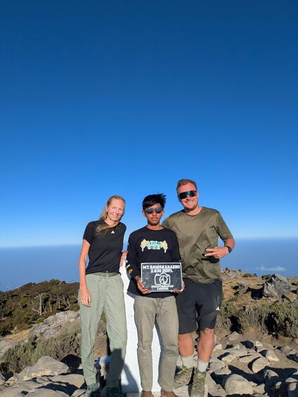 Three people standing on a rocky outcrop with a clear blue sky in the background. 5