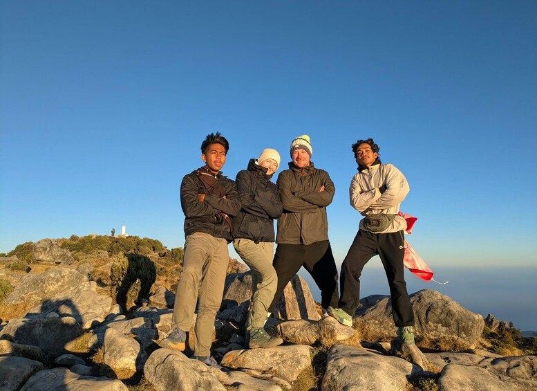 Four people standing on rocky terrain with a clear sky and a distant structure. 4
