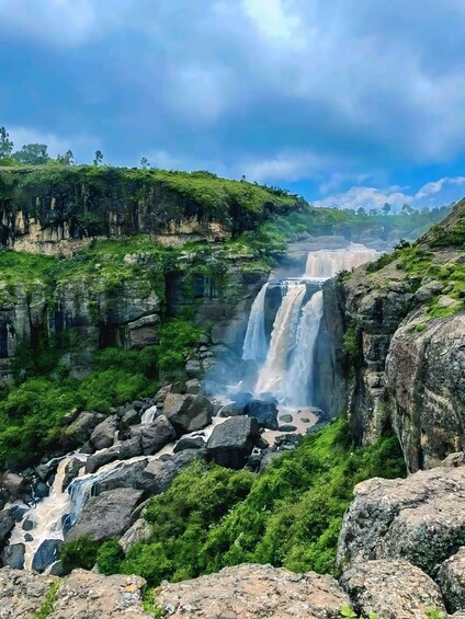 A multi-tiered waterfall surrounded by lush greenery and rocky terrain. 1