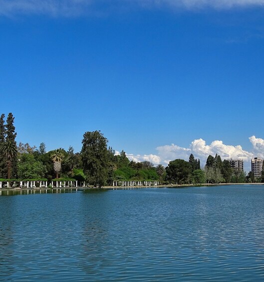 A calm lake with a clear blue sky, surrounded by lush greenery and white structures along the shore. 5