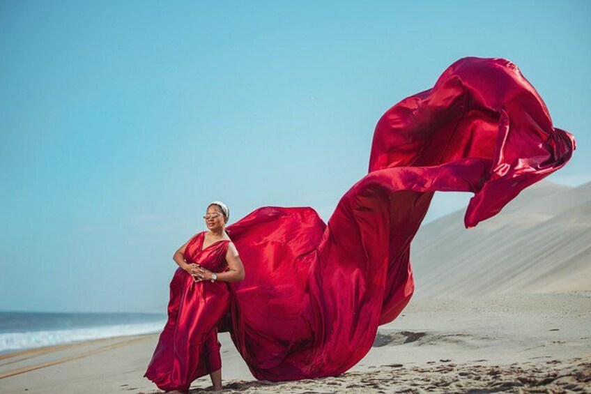 Eine Person in einem roten Kleid steht an einem Strand mit Dünen im Hintergrund. 2