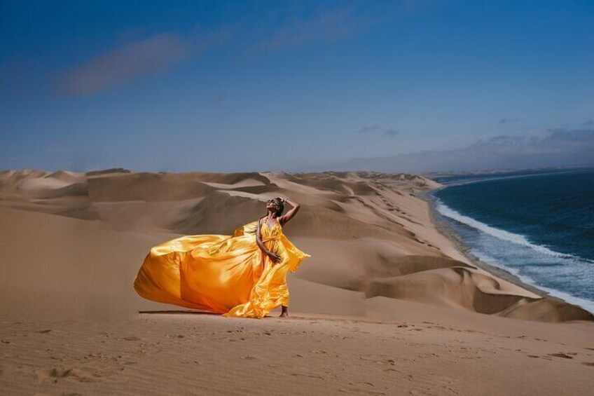 Een persoon in een zwierige gele jurk op een woest strand met duinen en de oceaan. 1