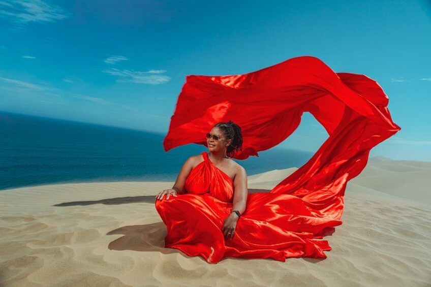 Eine Person sitzt am sandigen Strand, trägt ein rotes Kleid und ein fließendes, rotes Tuch. 4