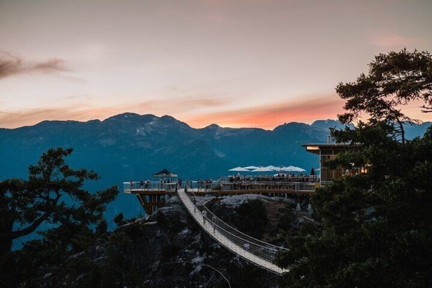 A mountain overlook with a wooden bridge and a restaurant with outdoor seating. 1