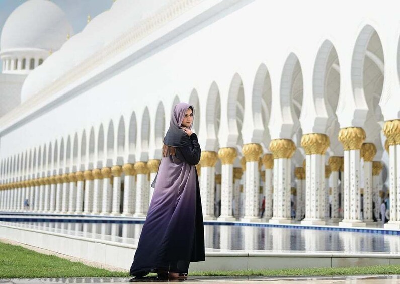 A person in a long dress standing in front of a white building with golden accents and arches. 5