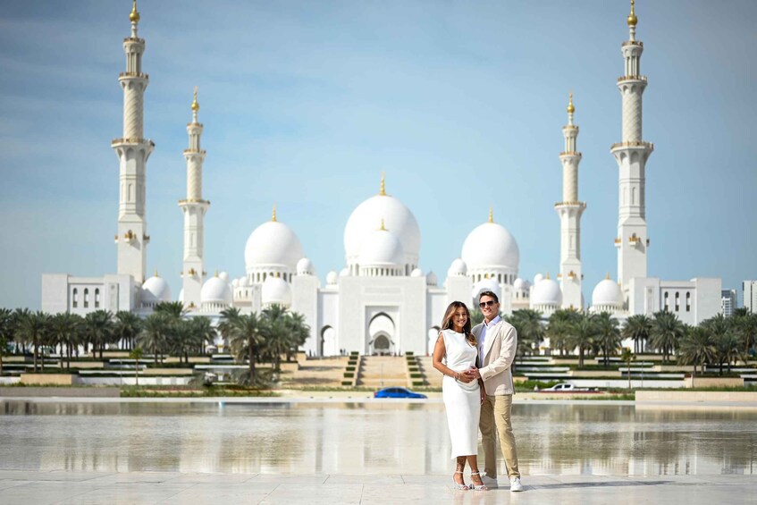A couple standing in front of a large white mosque with multiple domes and minarets. 2