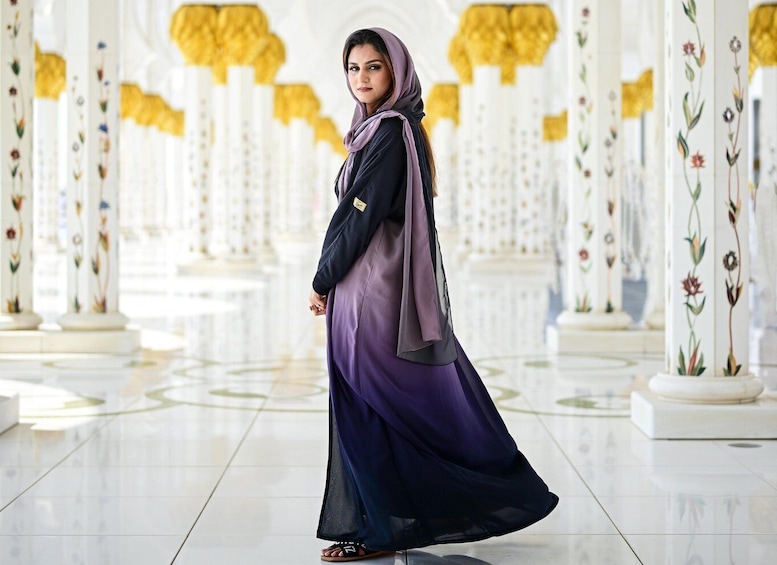 A woman in a purple and black dress walking in a grand, ornate hall with white columns and floral designs. 1