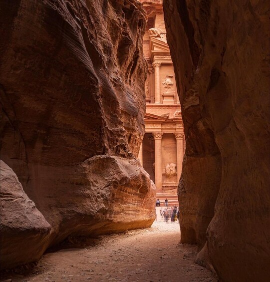 A narrow canyon with towering rock formations and a carved ancient structure in the background. 2