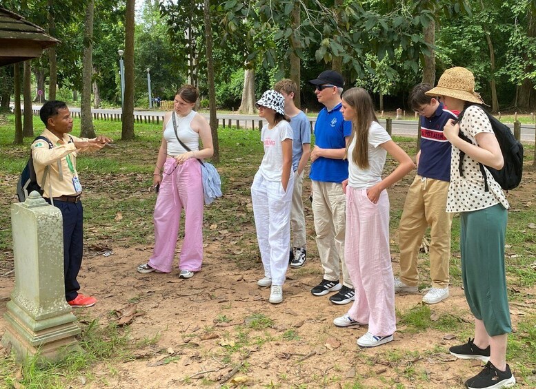 A group of people standing outdoors, some wearing hats, near a stone monument. 5
