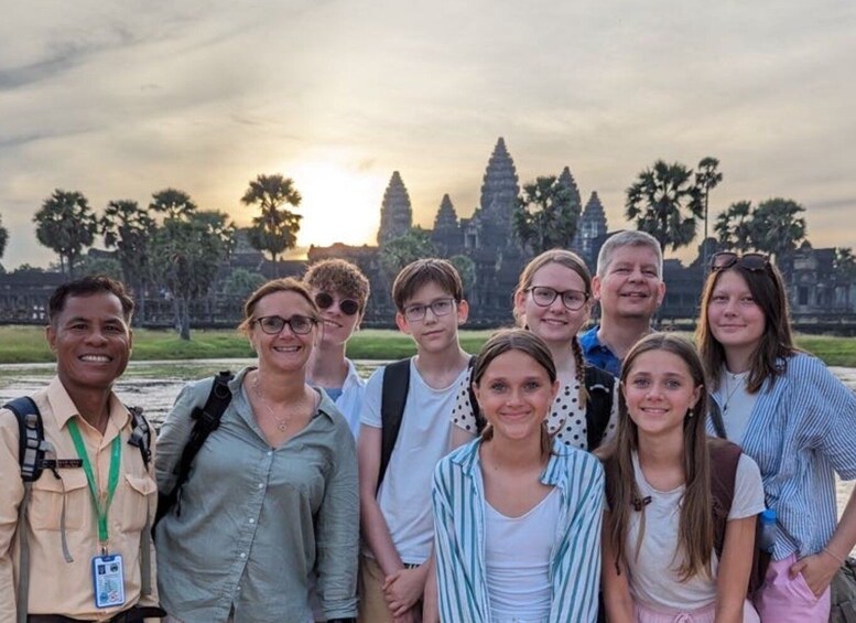 A group of people standing in front of Angkor Wat temple complex during sunset. 4