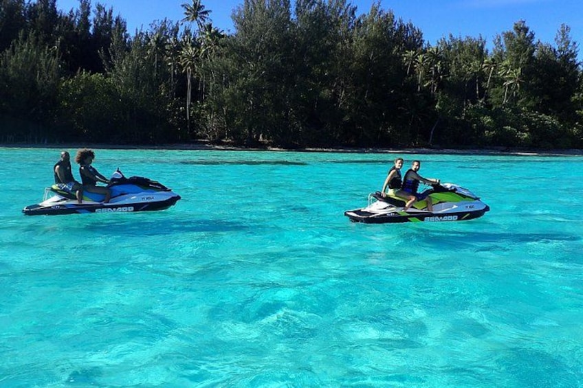 Due persone sulle moto d'acqua in acque turchesi, con un'isola ricoperta di vegetazione sullo sfondo. 1