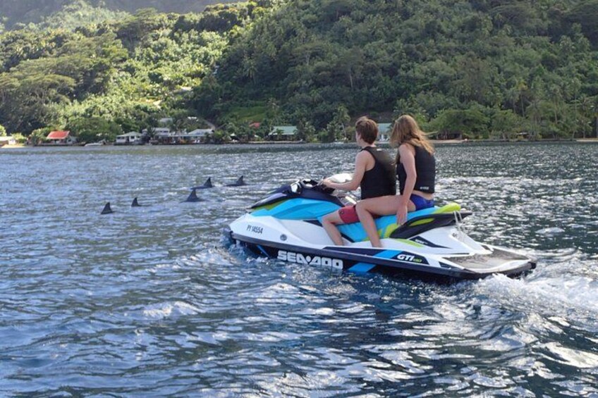 A jet ski with two people on it, moving on water with a forested shoreline in the background. 2