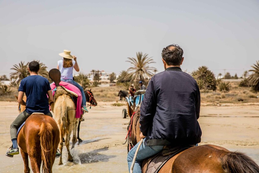 People riding horses on a beach with palm trees in the background. 2