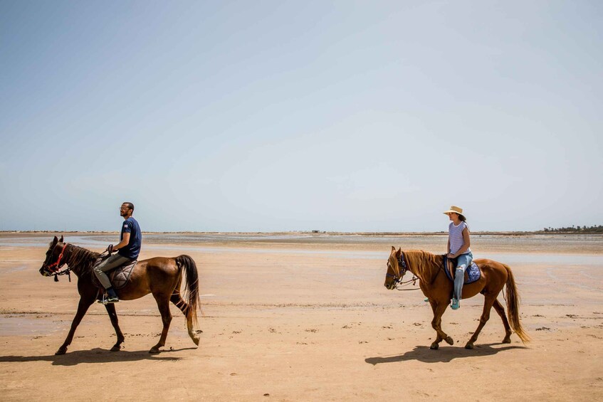 Two people riding horses on a sandy beach with a clear sky. 5