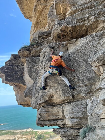 A person rock climbing a cliff with a clear view of the ocean and landscape below. 1